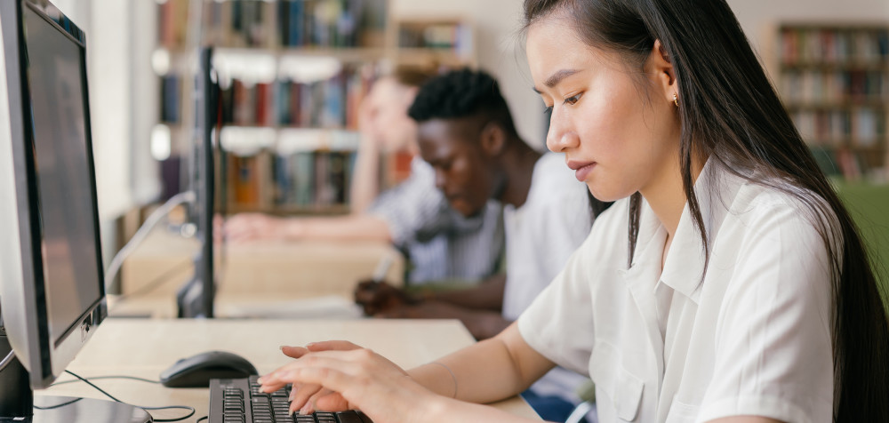 Eine junge Frau sitzt in einer Bibliothek und arbeitet an ihrem Laptop.