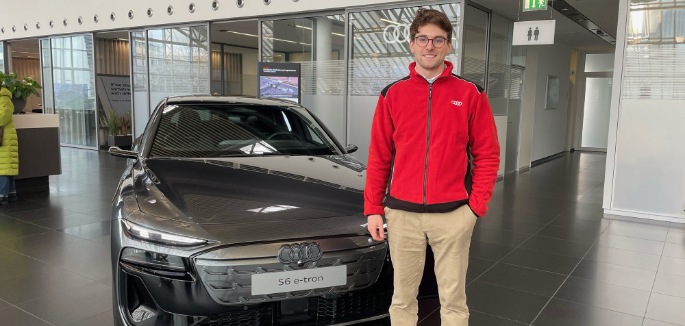 Junger Mann mit roter Jacke steht vor einem Luxusauto in einem Autohaus