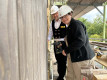 Frau und Mann sind gemeinsam auf einer Baustelle und bohren ein Loch in eine Holzwand.